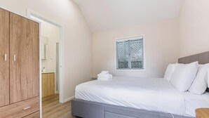 A bedroom with a bed, a wardrobe, a window with blinds, and a door leading to another room. - Serene 2BR Home w Grill & Yard by Zodiak Stays (Auckland)