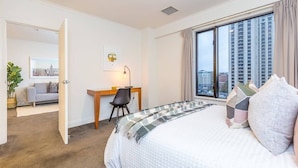 A hotel room with a large bed, a desk, and a view of the city through a large window.