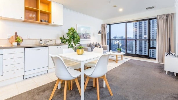 A modern kitchen with white cabinets, a dining area with a white table and chairs, and a large window with a city view.