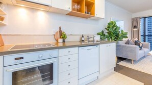 A modern kitchen with white cabinetry, a built-in oven, and a dishwasher. There is a countertop with a plant and a wine glass shelf above.
