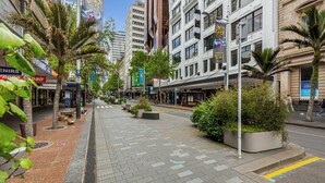 Een stadsstraat met palmbomen en moderne gebouwen, met een voetpad en diverse winkelpanden.