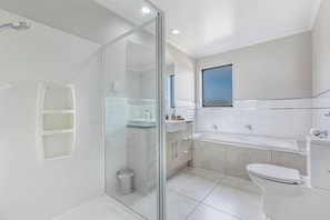 A modern bathroom with a glass shower enclosure, a large bathtub, and a toilet.