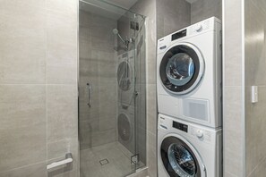 A modern bathroom with a glass-enclosed shower, a stacked washer and dryer, and a tiled floor. - Modern 2BR Penthouse for Families by Zodiak Stays (Auckland)