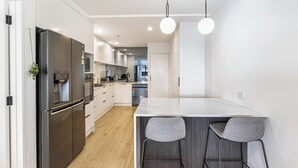 A modern kitchen with a large refrigerator, a marble countertop, and two bar stools.