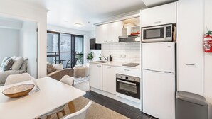 A modern kitchen with white cabinets, a microwave, oven, and a sink. There is a dining area with a table and chairs. - Central 3BR Full Kitchen & Amenities Zodiak Stays (Auckland)