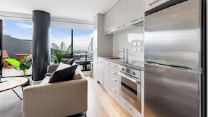 A modern kitchen with stainless steel appliances, a large window, and a balcony with outdoor seating. - Pool, Gym & Modern 2BR Sky Tower View Zodiak Stays (Auckland)