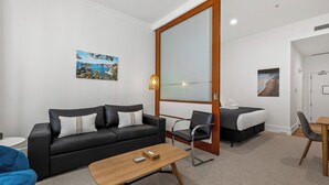 Ein modernes Hotelzimmer mit einer schwarzen Ledersofa, einem Holztisch, einem Einzelbett, einem Schreibtisch und einem großen Spiegel.