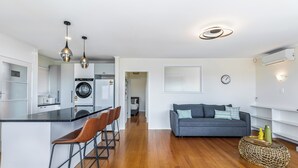 A modern kitchen with a central island, bar stools, and pendant lighting. A living area with a sofa and a round coffee table is visible in the background. - Serene 2BR Home in Meadowbank by Zodiak Stays (Auckland)