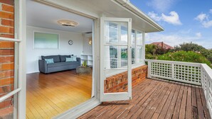 A wooden deck with a white railing, a grey sofa, and a brick wall. - Serene 2BR Home in Meadowbank by Zodiak Stays (Auckland)