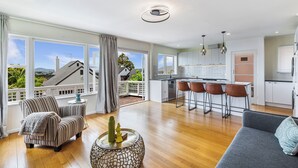A spacious living area with a sofa, striped armchair, and a round coffee table with decorative items. A kitchen with a bar and stools is visible through an open door. - Serene 2BR Home in Meadowbank by Zodiak Stays (Auckland)