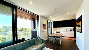 A modern living room with a sofa, dining table, and kitchen area. - 1BR with Balcony Close to Ferry by Zodiak Stays (Auckland)