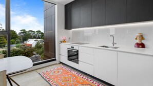 A modern kitchen with a large window, white cabinets, a built-in oven, and a sink. - 1BR with Balcony Close to Ferry by Zodiak Stays (Auckland)