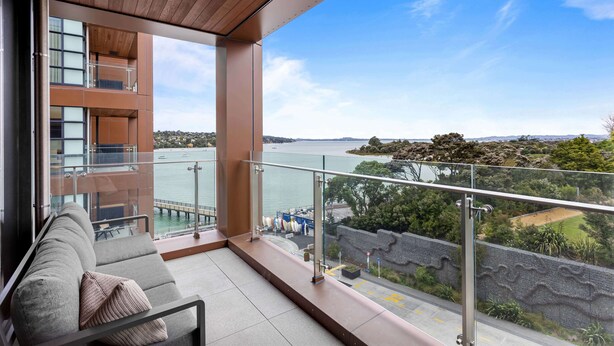 A balcony with a view of a body of water, a modern building, and a grassy area. - 1BR with Balcony Close to Ferry by Zodiak Stays (Auckland)