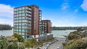 A modern multi-story building with a parking lot in front, overlooking a body of water with boats. - 1BR with Balcony Close to Ferry by Zodiak Stays (Auckland)