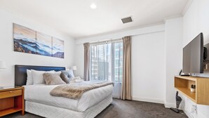 A modern hotel room with a large bed, a flat-screen TV, and a city view.