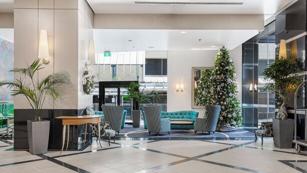 A modern lobby with a large Christmas tree, seating area, and a view of the street.