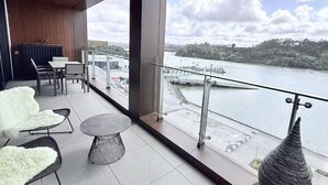 En moderne balkon med udsigt over en flod, møbleret med hvide stole og et rundt bord.