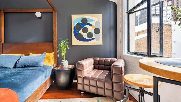 A modern bedroom with a bed, a seating area, and a window with a view of the city.