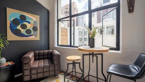 A modern room with a leather sofa, a small round table, and a black chair. A large window offers a view of buildings outside.