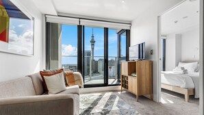 Habitación de hotel moderna con un amplio ventanal que ofrece vistas a la ciudad, un sofá, una cama, un televisor y un armario de madera.
