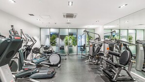 Et moderne fitnesscenter med diverse træningsmaskiner, store vinduer og planter indendørs.