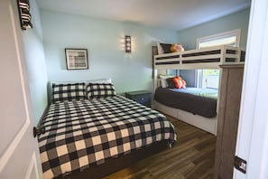 A bedroom with a bunk bed, a checkered bedspread, a small bedside table, and a wall-mounted light fixture. - North Conway Winter & Summer Retreat with Hot Tub & Fire Pit (Conway)