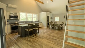 A spacious kitchen with wooden flooring, a central island, and a dining area with a staircase. - North Conway Winter & Summer Retreat with Hot Tub & Fire Pit (Conway)