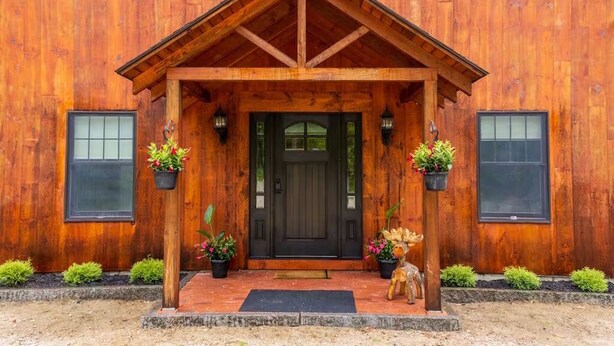 A wooden building with a dark front door, potted plants, and a small statue. - North Conway Winter & Summer Retreat with Hot Tub & Fire Pit (Conway)