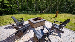 A patio with Adirondack chairs and a stone fire pit. - North Conway Winter & Summer Retreat with Hot Tub & Fire Pit (Conway)