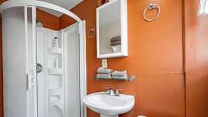 Une salle de bain avec une baignoire blanche, un lavabo blanc et des toilettes. On y trouve un rideau de douche, un porte-serviettes et une étagère avec des serviettes.