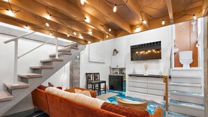 Un salon moderne avec un escalier, un canapé, un téléviseur et un coin cuisine.