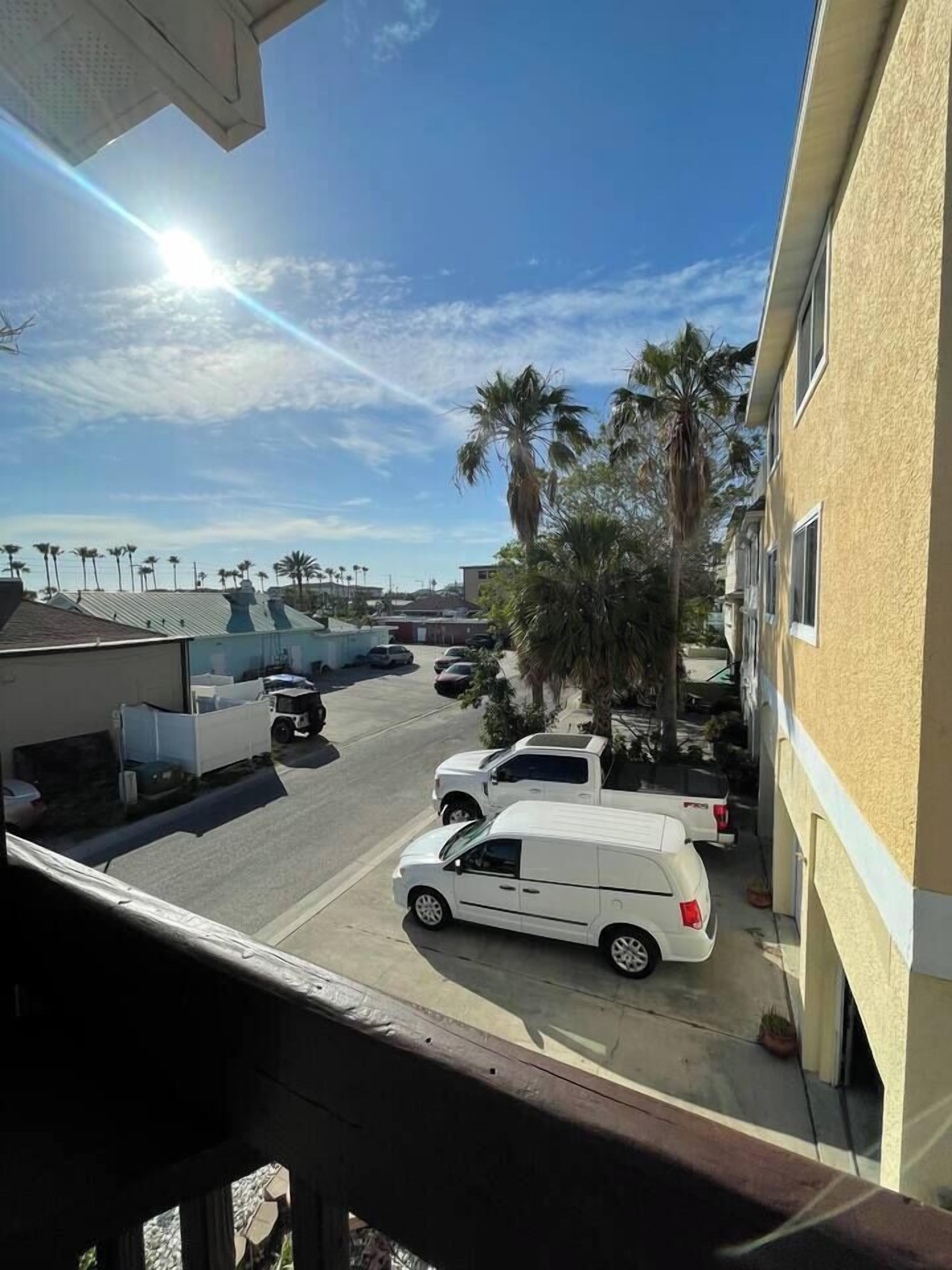 Un estacionamiento con varios vehículos blancos, palmeras y un cielo despejado.