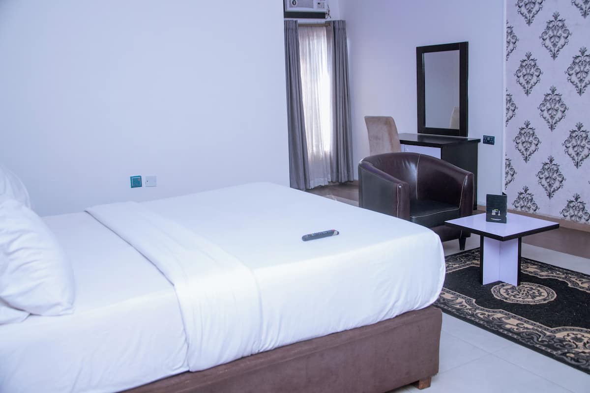 A hotel room with a bed, a chair, a small table, and a mirror.