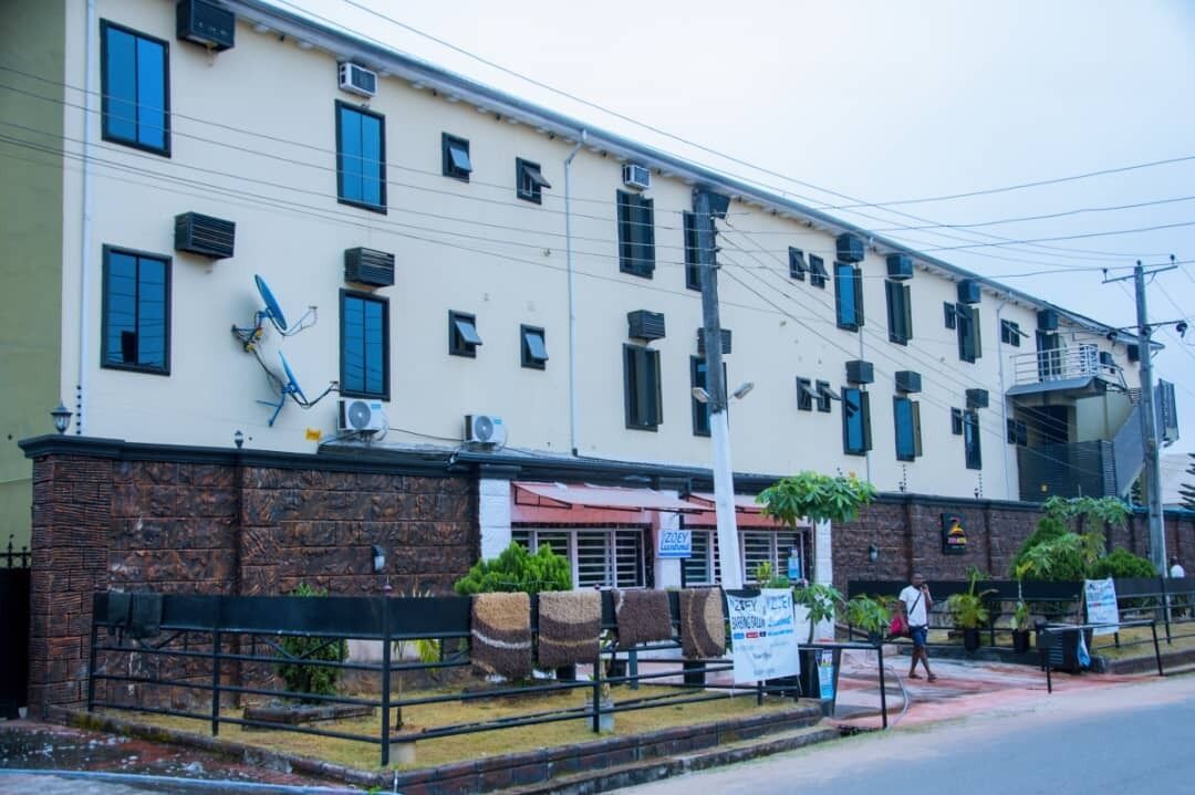 A multi-story building with a beige facade, multiple air conditioning units, and a brick base.