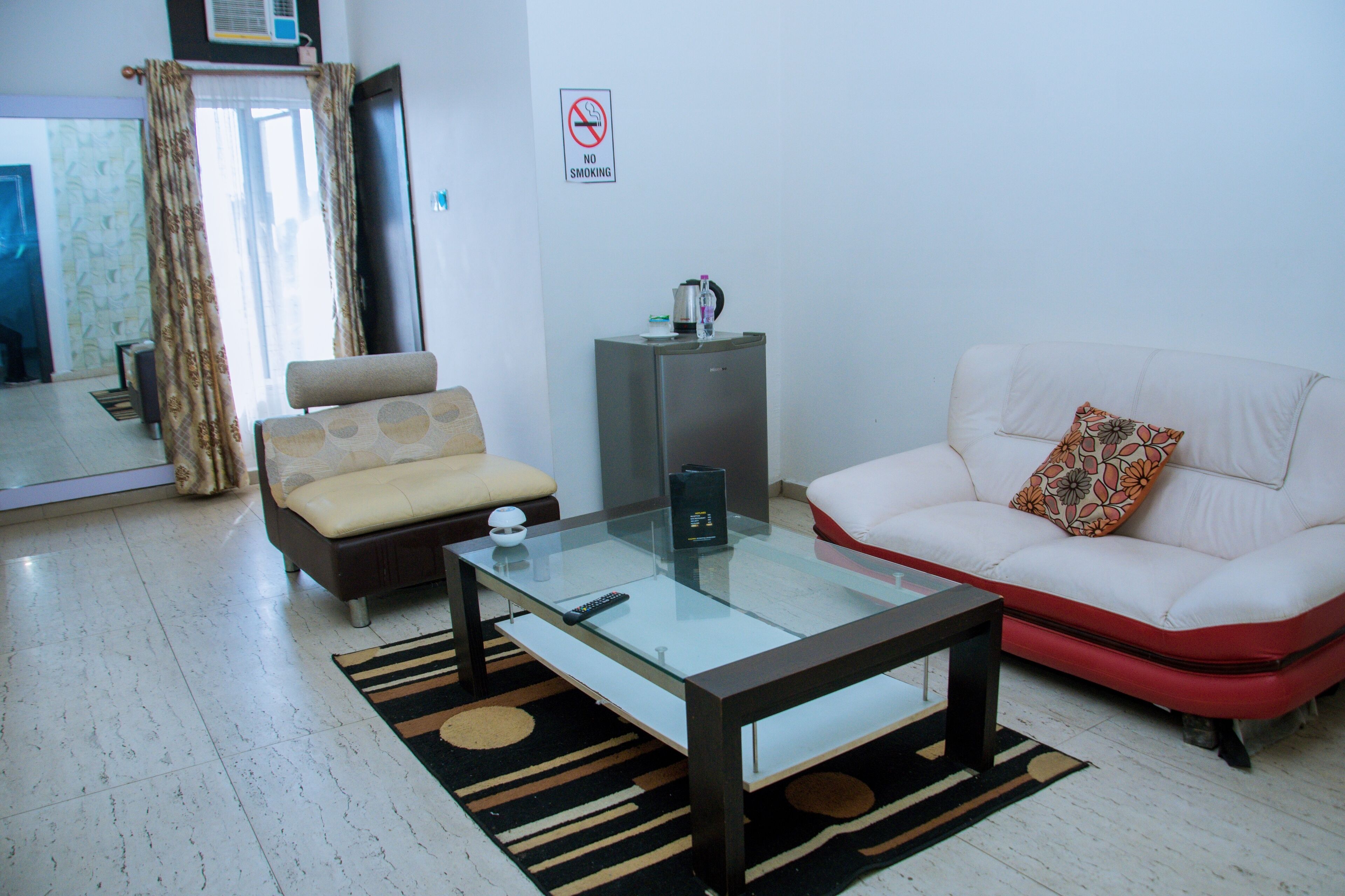 Una sala de estar con una mesa de centro de vidrio, un sofá, un mueble bajo y un cartel de prohibido fumar en la pared.