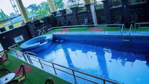 Una piscina con revestimiento de azulejos azules, rodeada de muros de piedra y una zona con césped y sillas.