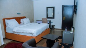 Un dormitorio con cama, escritorio, silla, mesita, espejo y puerta.