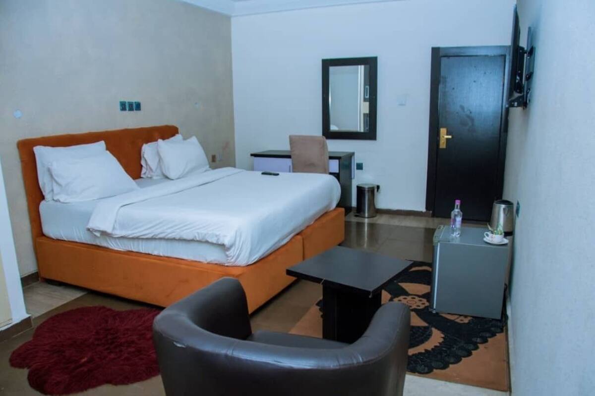 A bedroom with a bed, a desk, a chair, a small table, a mirror, and a door.