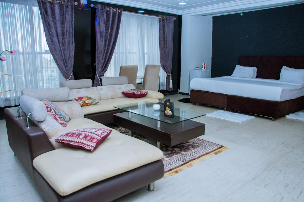 A modern hotel room with a sofa, a glass coffee table, a bed, and a large window with curtains.