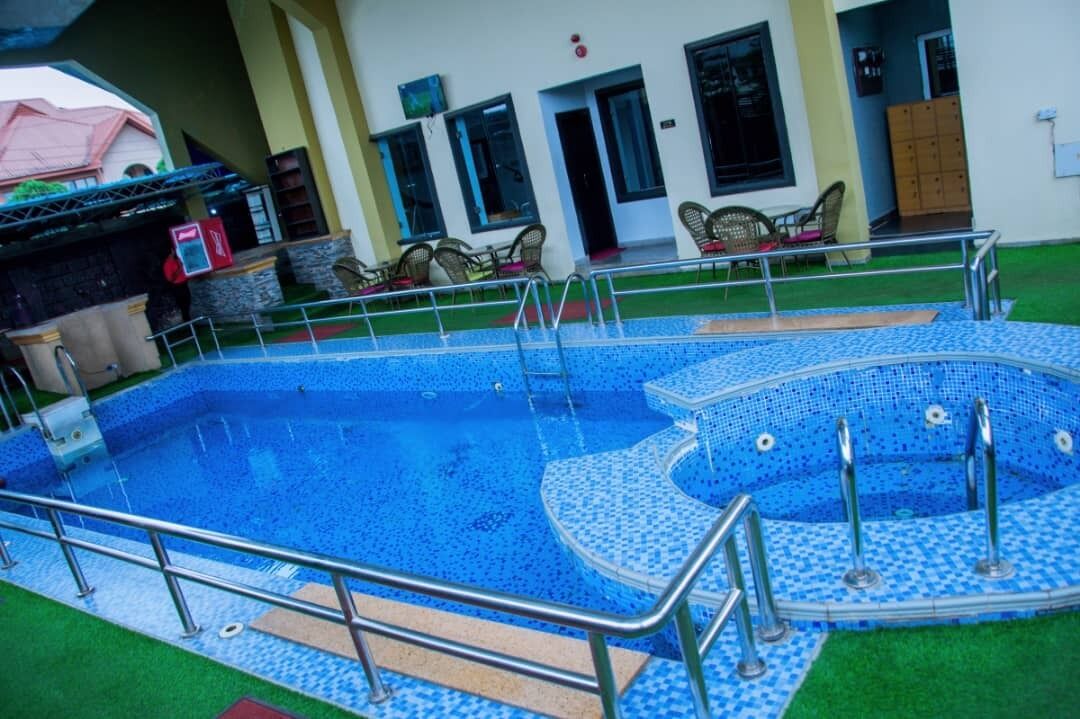 A swimming pool with a tiled deck and metal railings, surrounded by a building with multiple doors and windows.