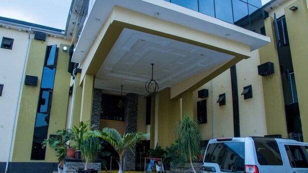 Un edificio moderno con vestíbulo cubierto, plantas en macetas y un SUV estacionado.
