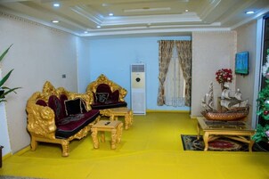 Una habitación con piso amarillo, dos sofás dorados ornamentados con cojines rojos, una mesita pequeña, un modelo de barco y un árbol de Navidad.
