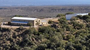 A building with a flat roof and a fenced area, surrounded by sparse vegetation and distant mountains. - Spacious 6-bedroom hilltop cabin in tranquil Oracle (Oracle)