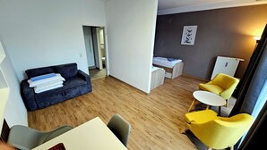 Un salon moderne avec un canapé bleu foncé, un fauteuil jaune, une petite table blanche et un plancher en bois.