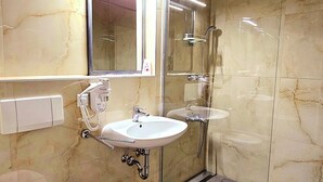 Une salle de bain moderne avec un mur en marbre, une cabine de douche en verre, un lavabo blanc et des toilettes.