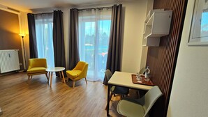 Une pièce comprenant deux fauteuils jaunes, une petite table ronde, une table à manger avec des chaises et un radiateur.