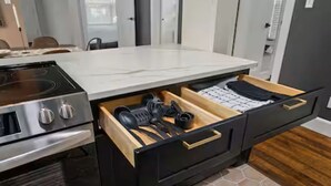A kitchen with a built-in stove, a drawer with kitchen utensils, and a tiled backsplash.