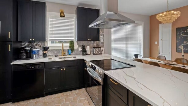 A modern kitchen with dark cabinetry, a central island, a built-in oven, and a large window with blinds.