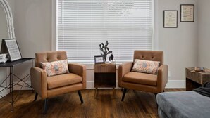 A room with two brown leather armchairs, a small wooden side table, and a large window with blinds.