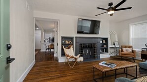 A living room with a fireplace, a television mounted above it, and a ceiling fan.
